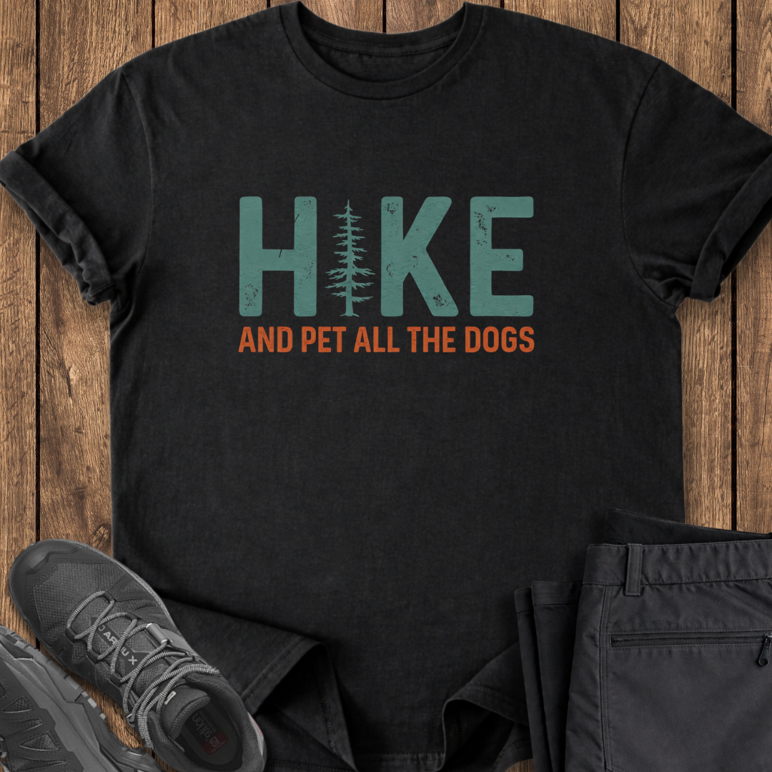 Black t-shirt with 'Hike and Pet All the Dogs' text on a wooden surface with shoes and pants. dog lover hiking tee