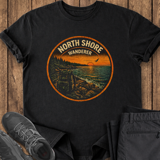 Black t-shirt with 'North Shore Wanderer' graphic design on a wooden surface with shoes and pants. superior hiking trail