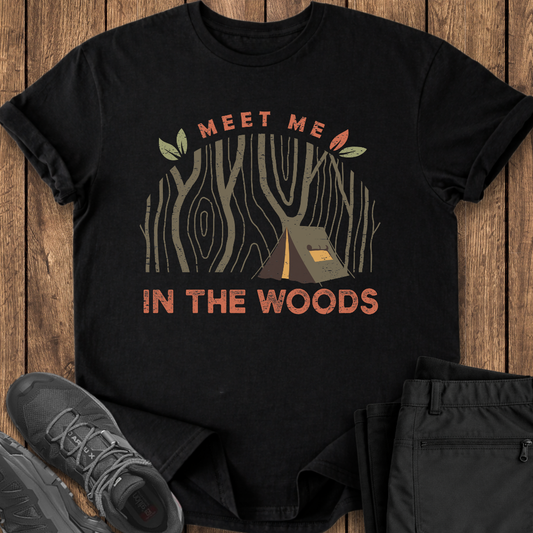 Black t-shirt with 'Meet Me in the Woods' design on a wooden surface with shoes and pants.