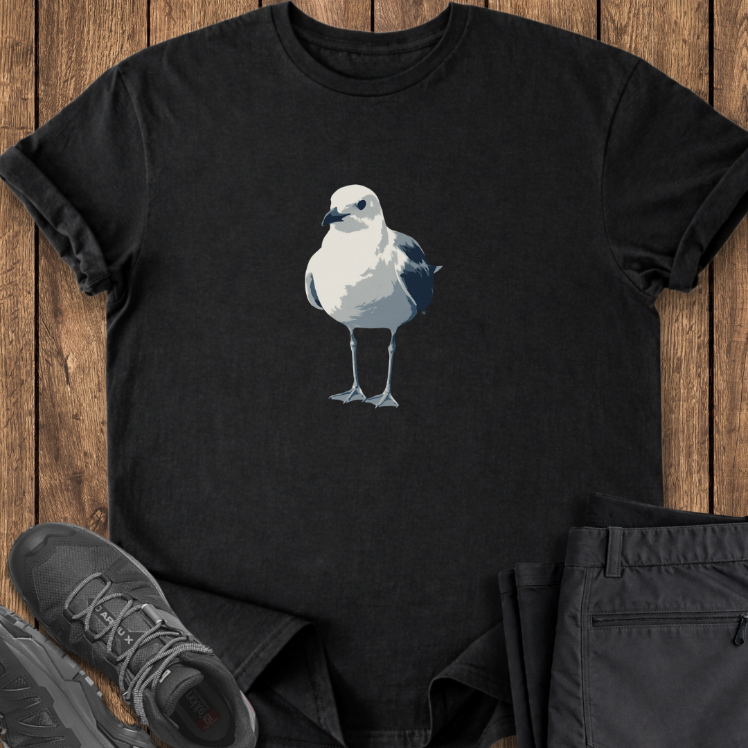 Black t-shirt with a seagull design on a wooden surface with shoes and pants.