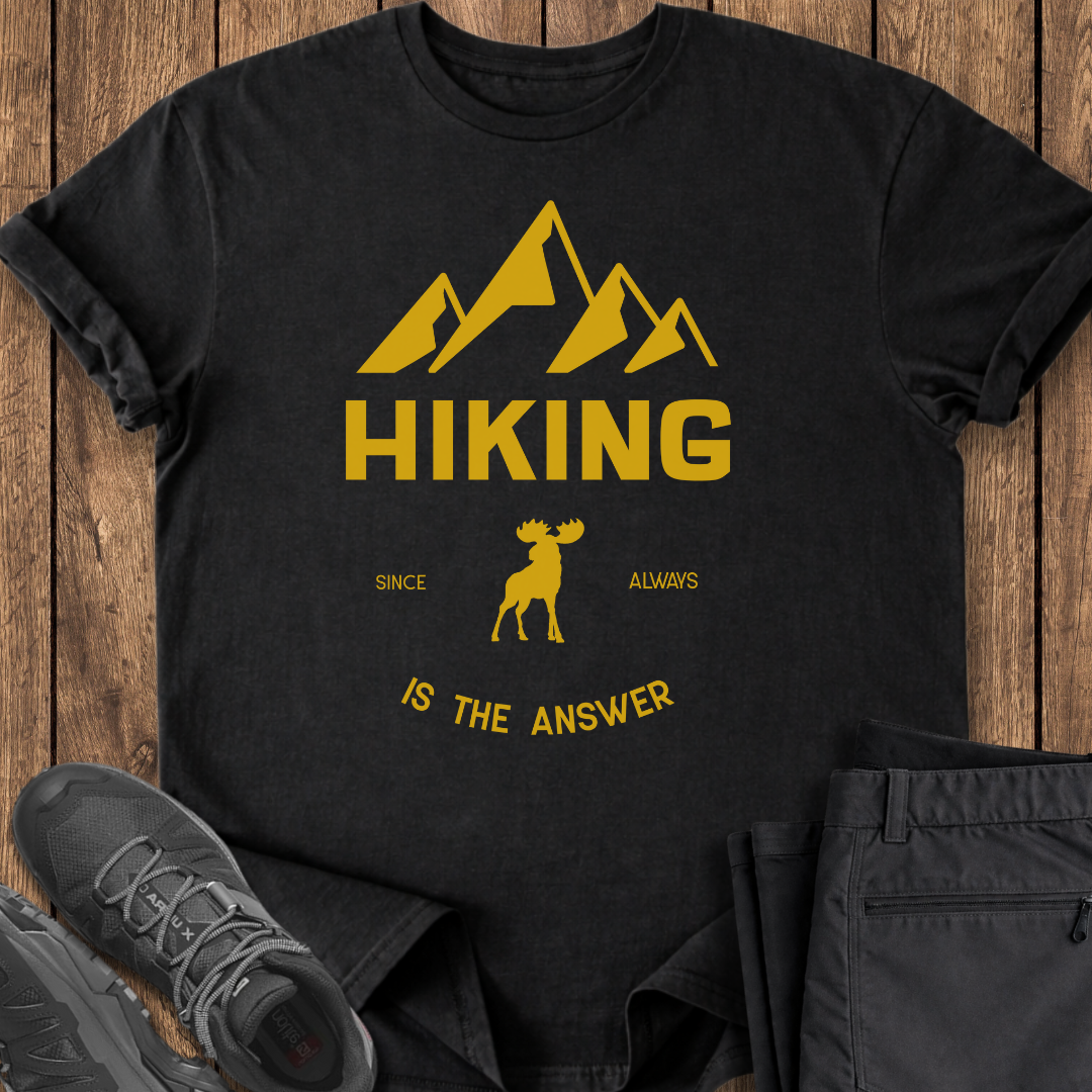 Black t-shirt with yellow mountain and moose design on a wooden surface with shoes and pants. funny hiking shirt