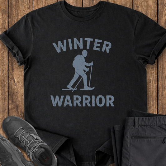Black t-shirt with 'Winter Warrior' graphic on a wooden surface with shoes and pants.