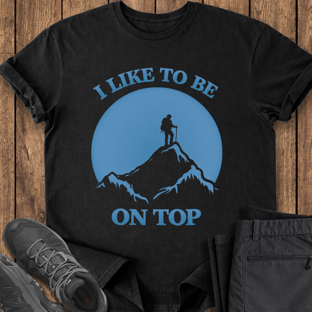 Black t-shirt with mountain and hiker graphic and text 'I Like to be on Top' on a wooden surface. funny mountain hiking t shirt