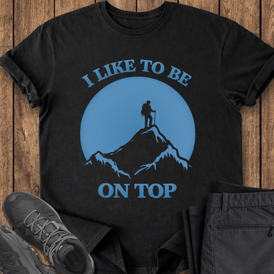 Black t-shirt with mountain and hiker graphic and text 'I Like to be on Top' on a wooden surface. funny mountain hiking t shirt