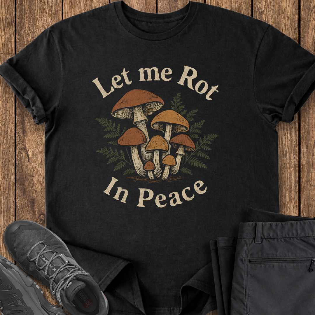 Black t-shirt with mushroom design and text 'Let me Rot In Peace' on a wooden surface.