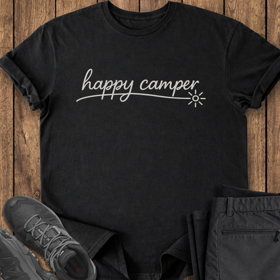Black t-shirt with 'happy camper' text on a wooden surface with shoes and pants.