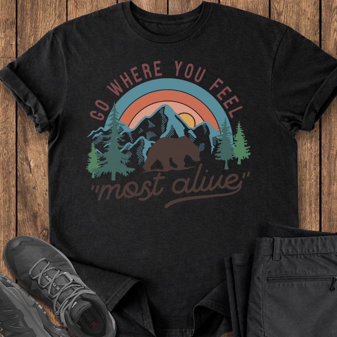 Black t-shirt with nature graphic and text on a wooden surface with shoes and pants.