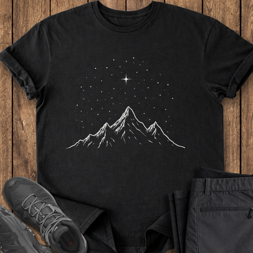 Black t-shirt with mountain and star design on a wooden surface with shoes and pants.
