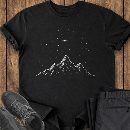 Black t-shirt with mountain and star design on a wooden surface with shoes and pants.