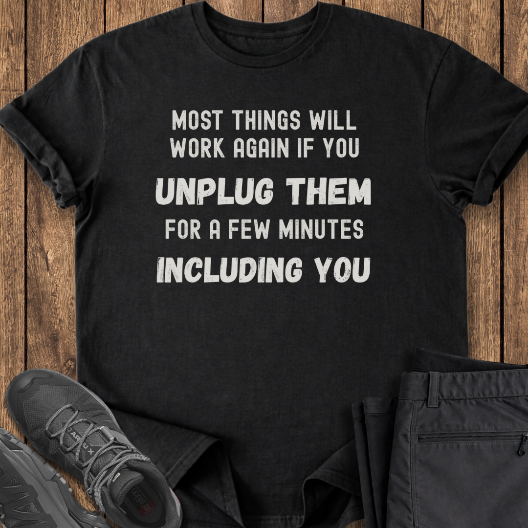 Black t-shirt with humorous text on a wooden surface with shoes and pants.