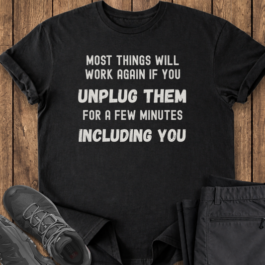 Black t-shirt with humorous text on a wooden surface with shoes and pants.