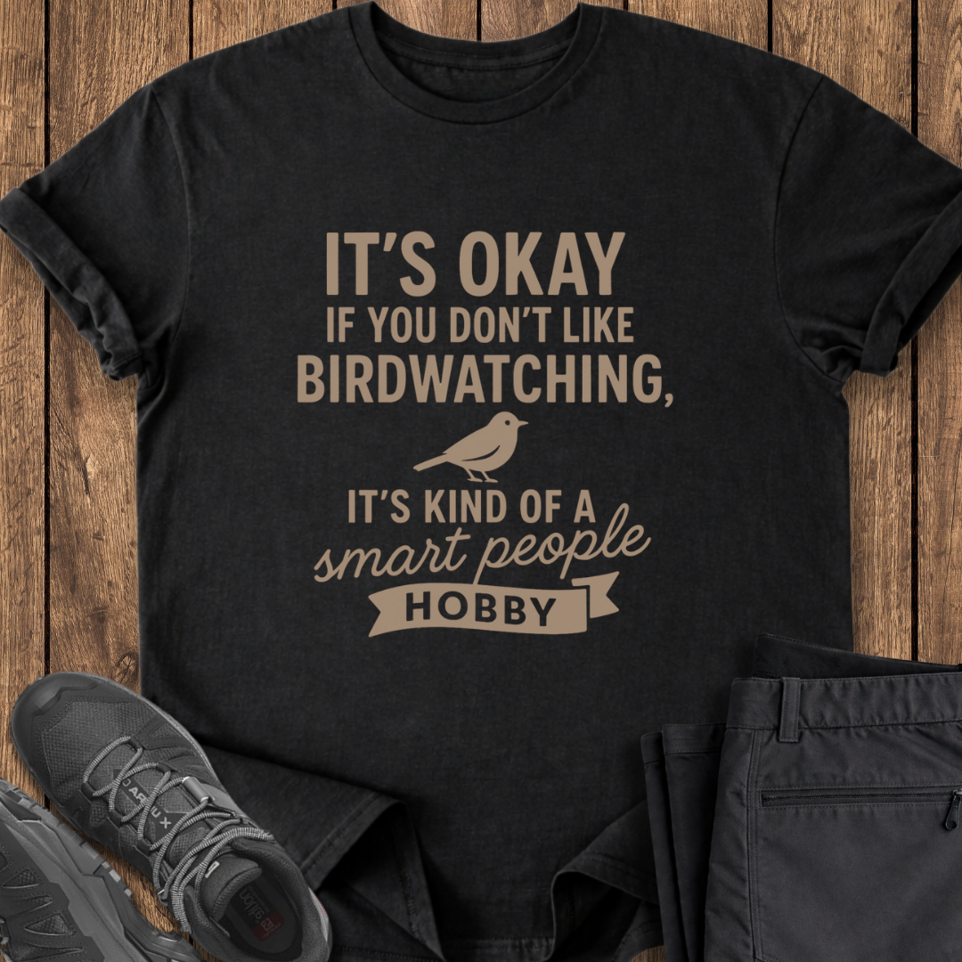 Black t-shirt with humorous text design on a wooden surface with shoes and pants.