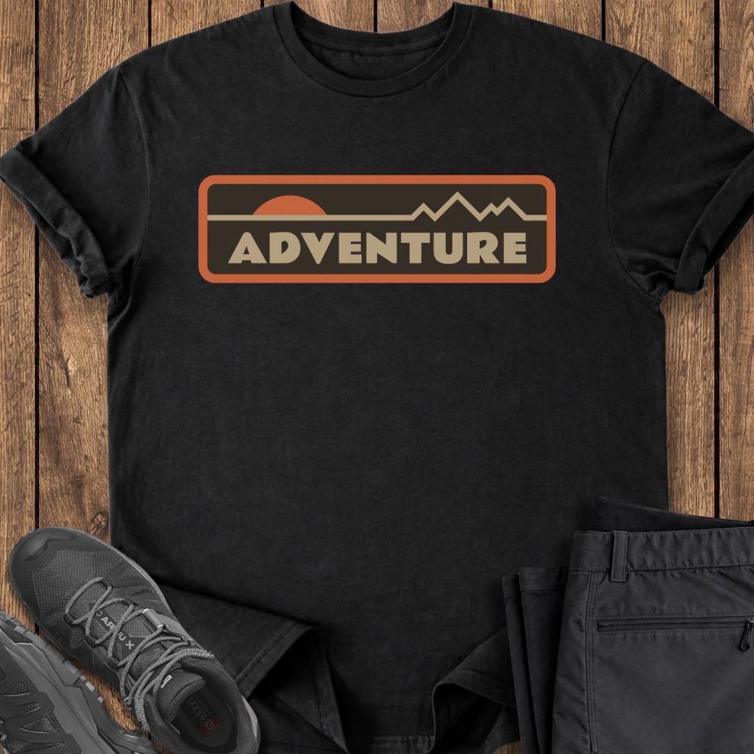 Black t-shirt with 'ADVENTURE' graphic on a wooden surface with shoes and pants.