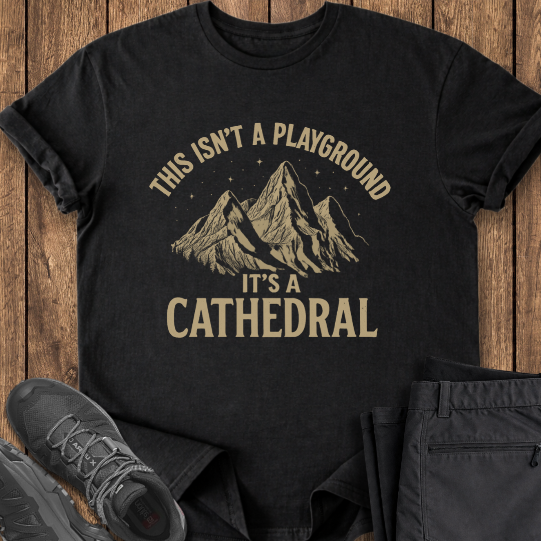 Black t-shirt with mountain graphic and text on a wooden surface with shoes and pants.