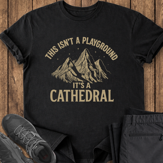 Black t-shirt with mountain graphic and text on a wooden surface with shoes and pants.