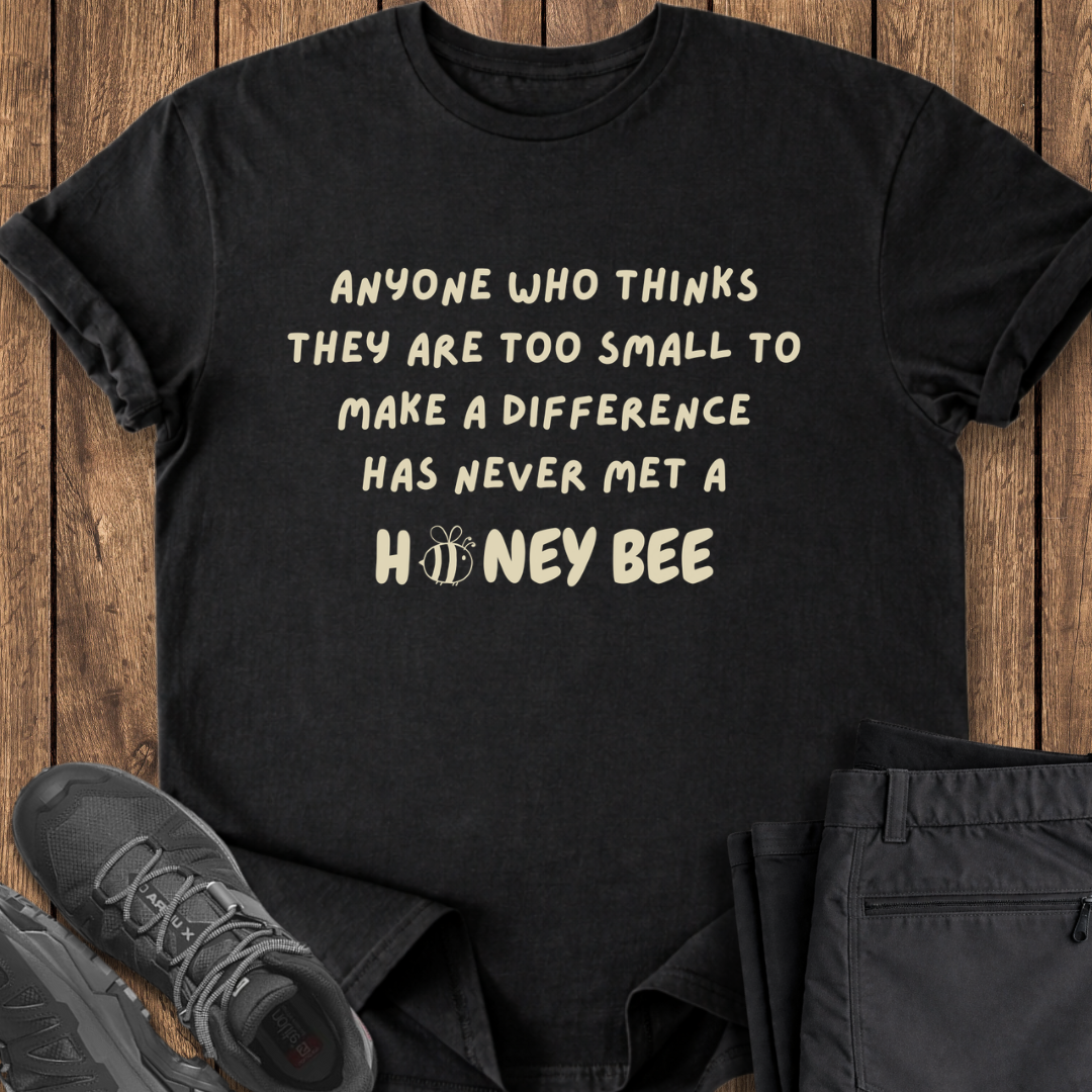 Black t-shirt with motivational quote on a wooden surface with shoes and pants. conservation stewardship bee t shirt