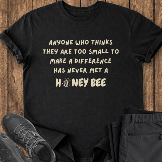 Black t-shirt with motivational quote on a wooden surface with shoes and pants. conservation stewardship bee t shirt
