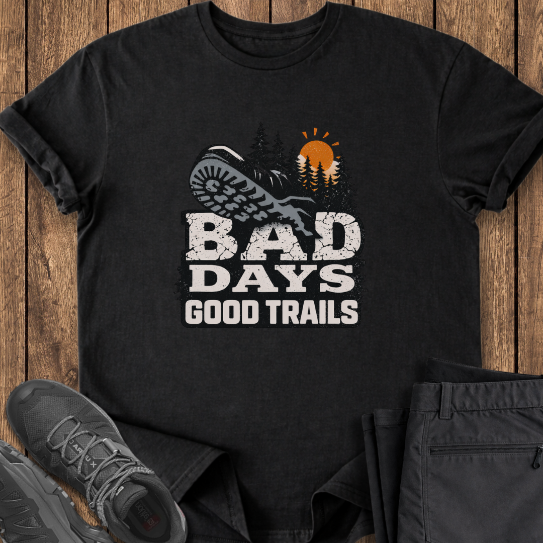 Black t-shirt with 'Bad Days Good Trails' graphic on a wooden surface with shoes and pants. mental health hiking t shirt