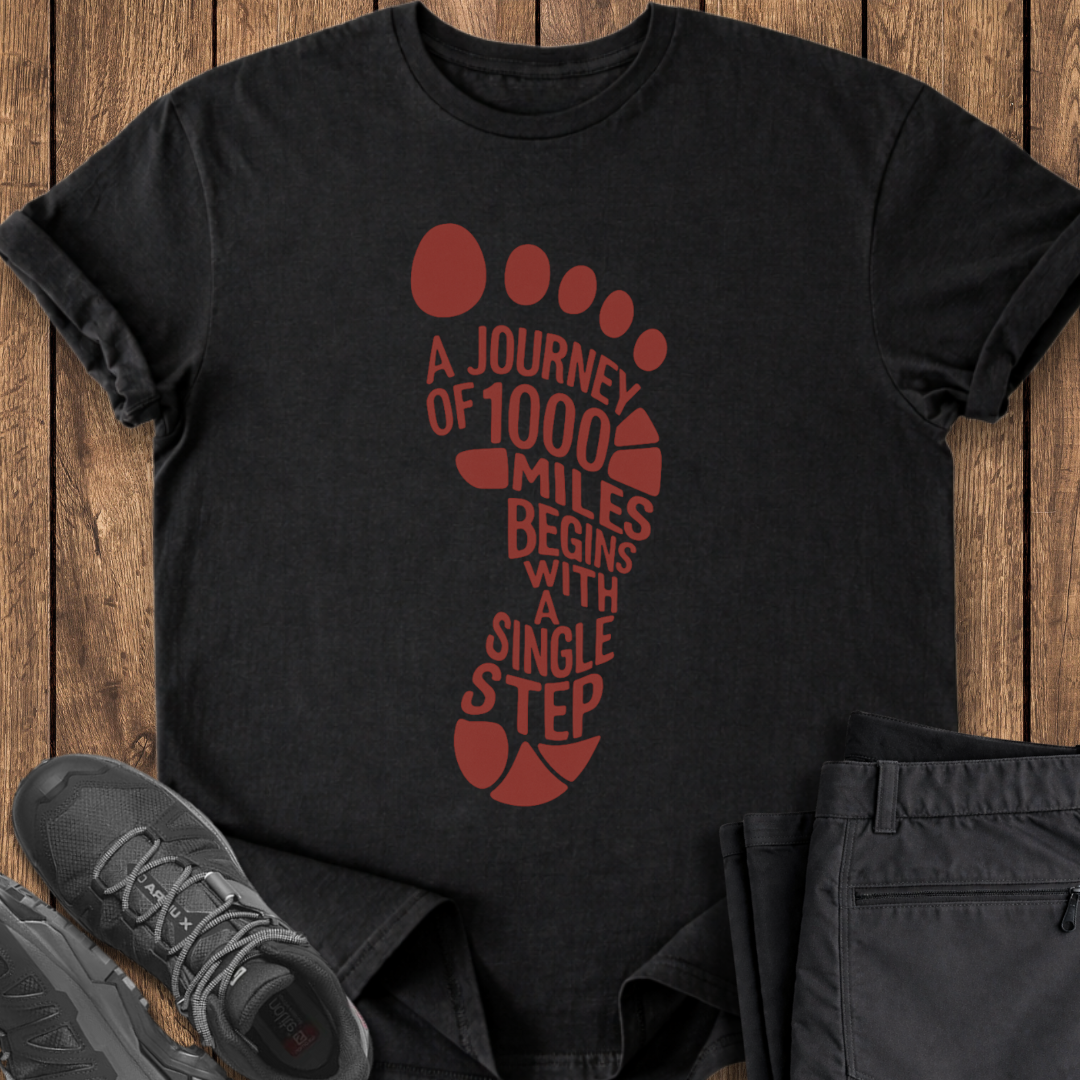 Black t-shirt with red footprint design and text on a wooden surface with shoes and pants.