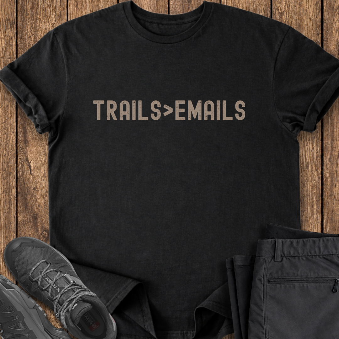 Black t-shirt with 'TRAILS>EMAILS' text on a wooden surface with shoes and pants.