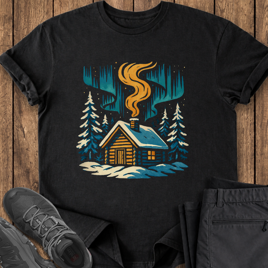 Black t-shirt with a cabin graphic on a wooden surface with shoes and pants.