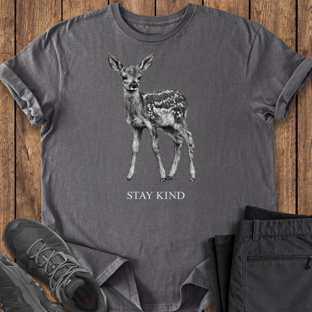 Gray t-shirt with a deer graphic and 'Stay Kind' text on a wooden surface, with shoes and pants partially visible.
