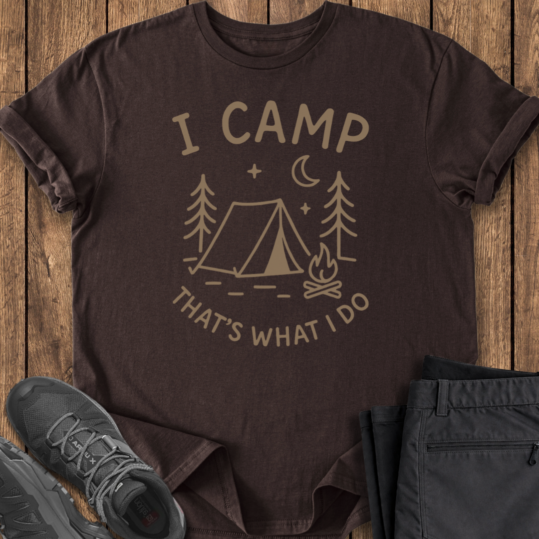 Brown t-shirt with 'I Camp, That's What I Do' design on a wooden surface with shoes and pants.
