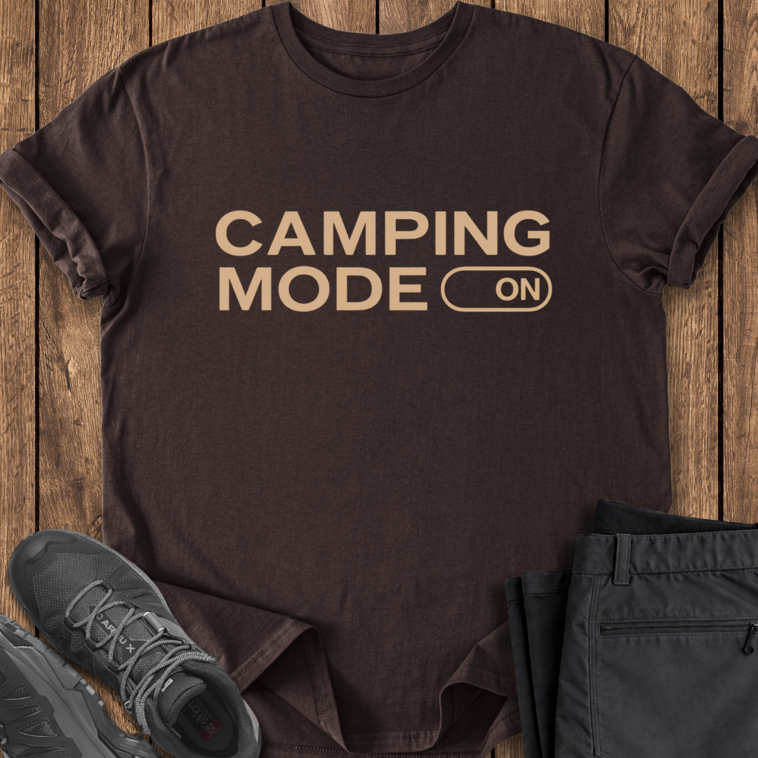 Brown t-shirt with 'Camping Mode On' text on a wooden surface with shoes and pants.