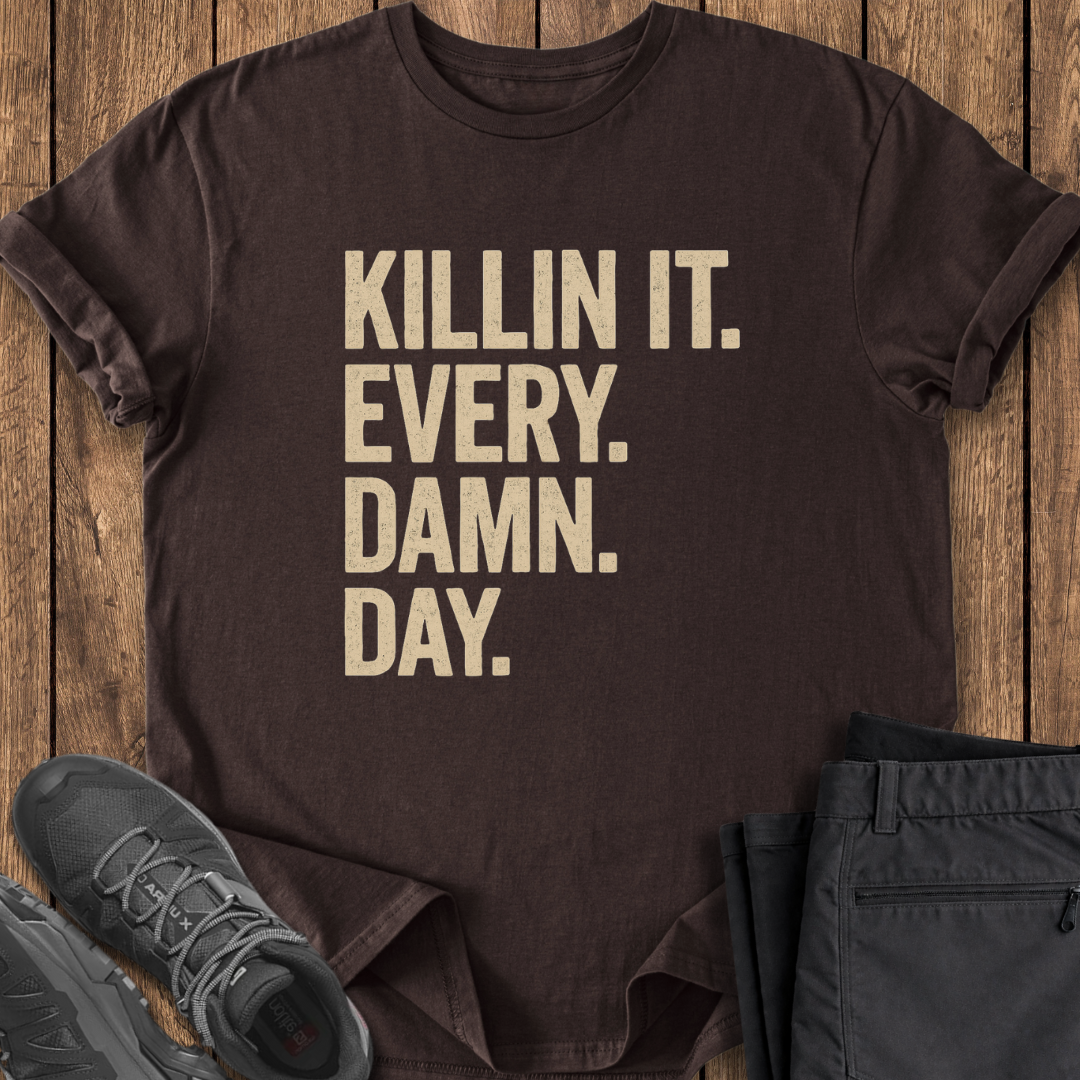 Brown t-shirt with 'KILLIN IT. EVERY. DAMN. DAY.' text on a wooden surface with shoes and pants.