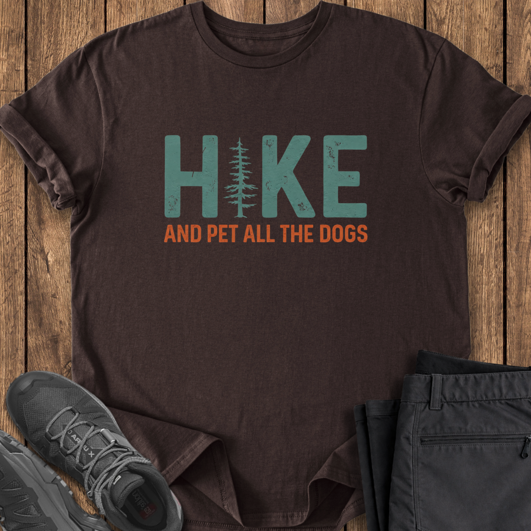Brown t-shirt with 'Hike and Pet All the Dogs' text on a wooden surface with shoes and pants. dog lover hiking tee