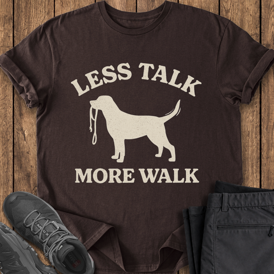 Brown t-shirt with a dog graphic and text 'LESS TALK MORE WALK' on a wooden surface.