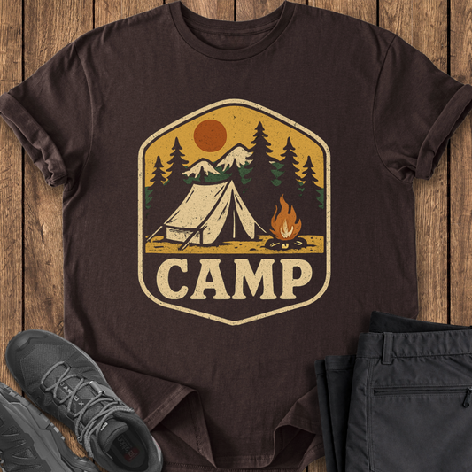 Brown t-shirt with 'CAMP' graphic on a wooden surface with shoes and pants.