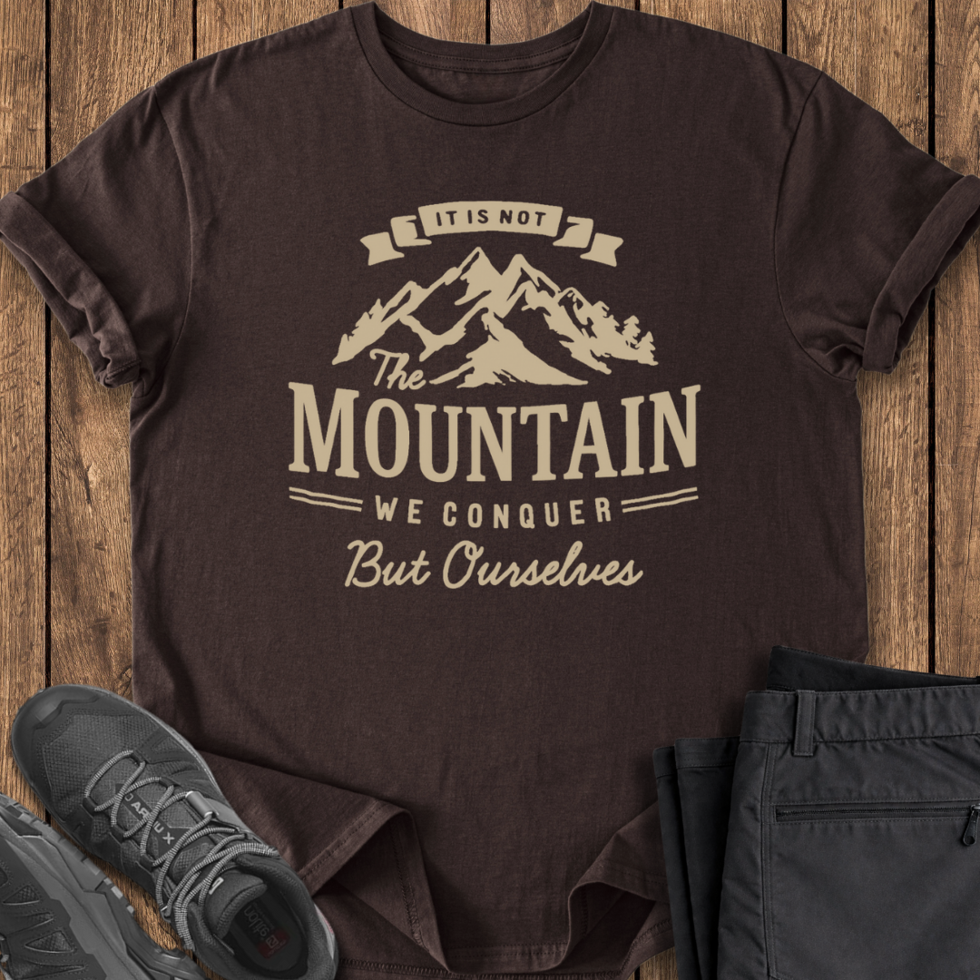 Brown t-shirt with mountain graphic and text on a wooden surface with shoes and pants.