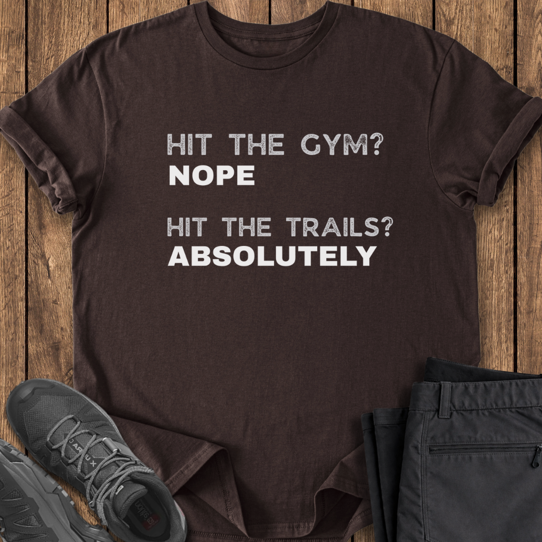 Brown t-shirt with humorous text on a wooden surface with shoes and pants.