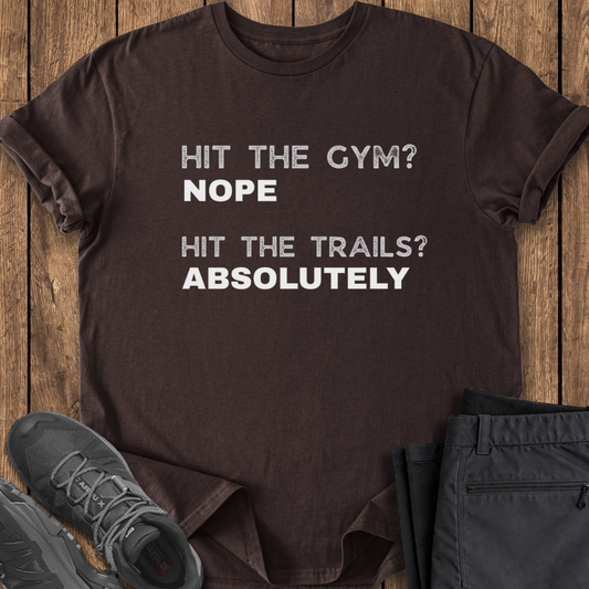 Brown t-shirt with humorous text on a wooden surface with shoes and pants.