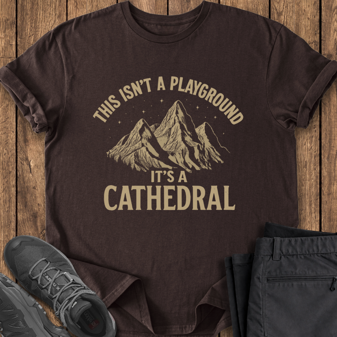 Brown t-shirt with mountain graphic and text on a wooden surface with shoes and pants.