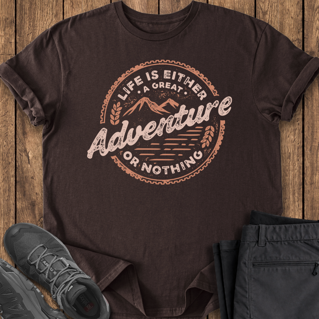 Brown t-shirt with 'Life is Either a Great Adventure or Nothing' text on a wooden surface with shoes and pants.