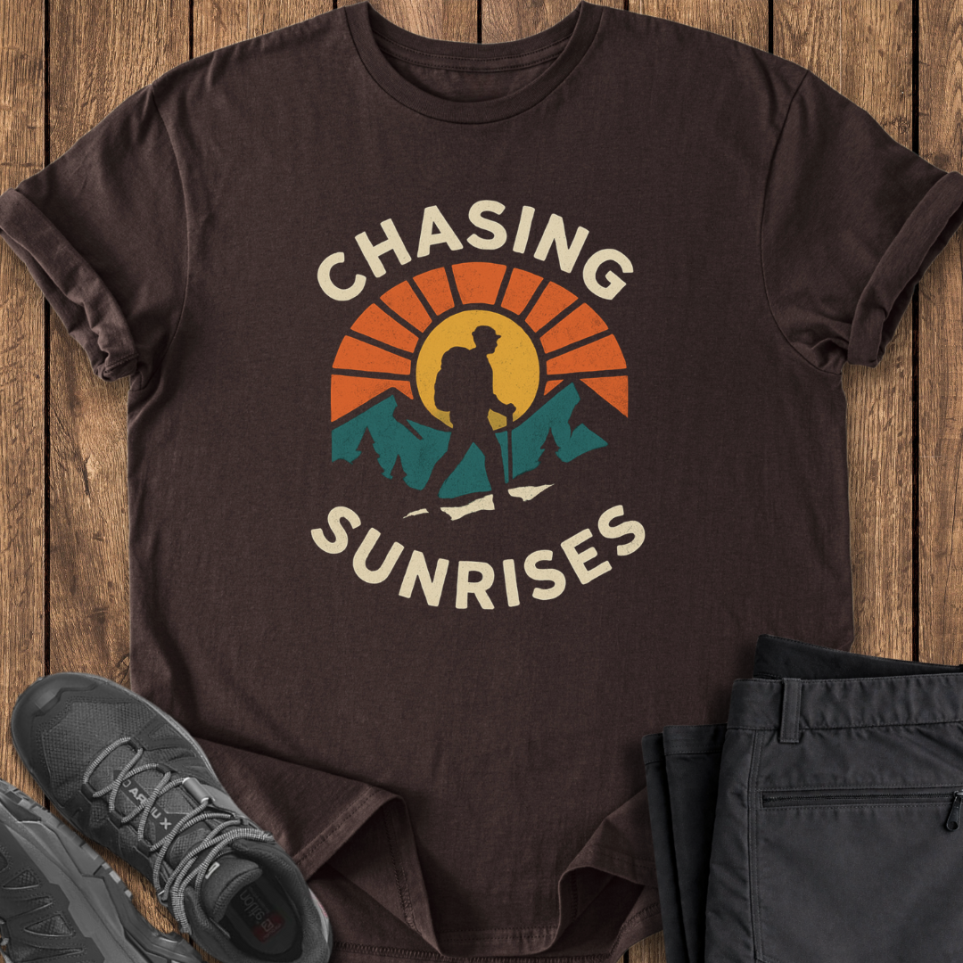 Brown t-shirt with 'Chasing Sunrises' graphic on a wooden surface with shoes and pants.
