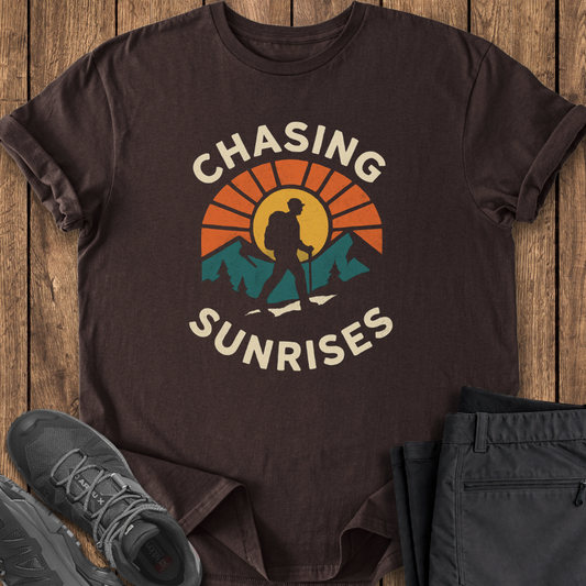 Brown t-shirt with 'Chasing Sunrises' graphic on a wooden surface with shoes and pants.