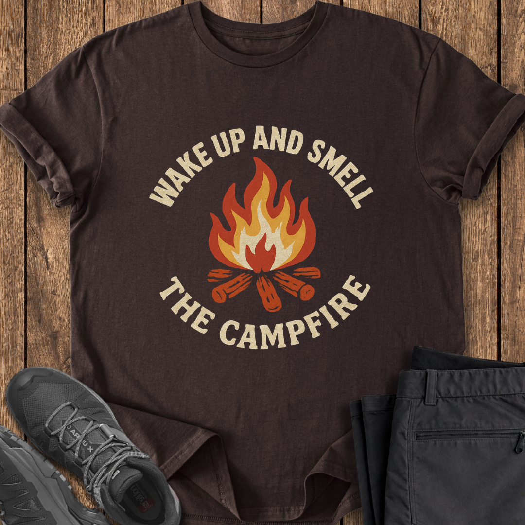 Brown t-shirt with 'Wake Up and Smell the Campfire' design on a wooden surface with shoes and pants. funny camping camp t shirts