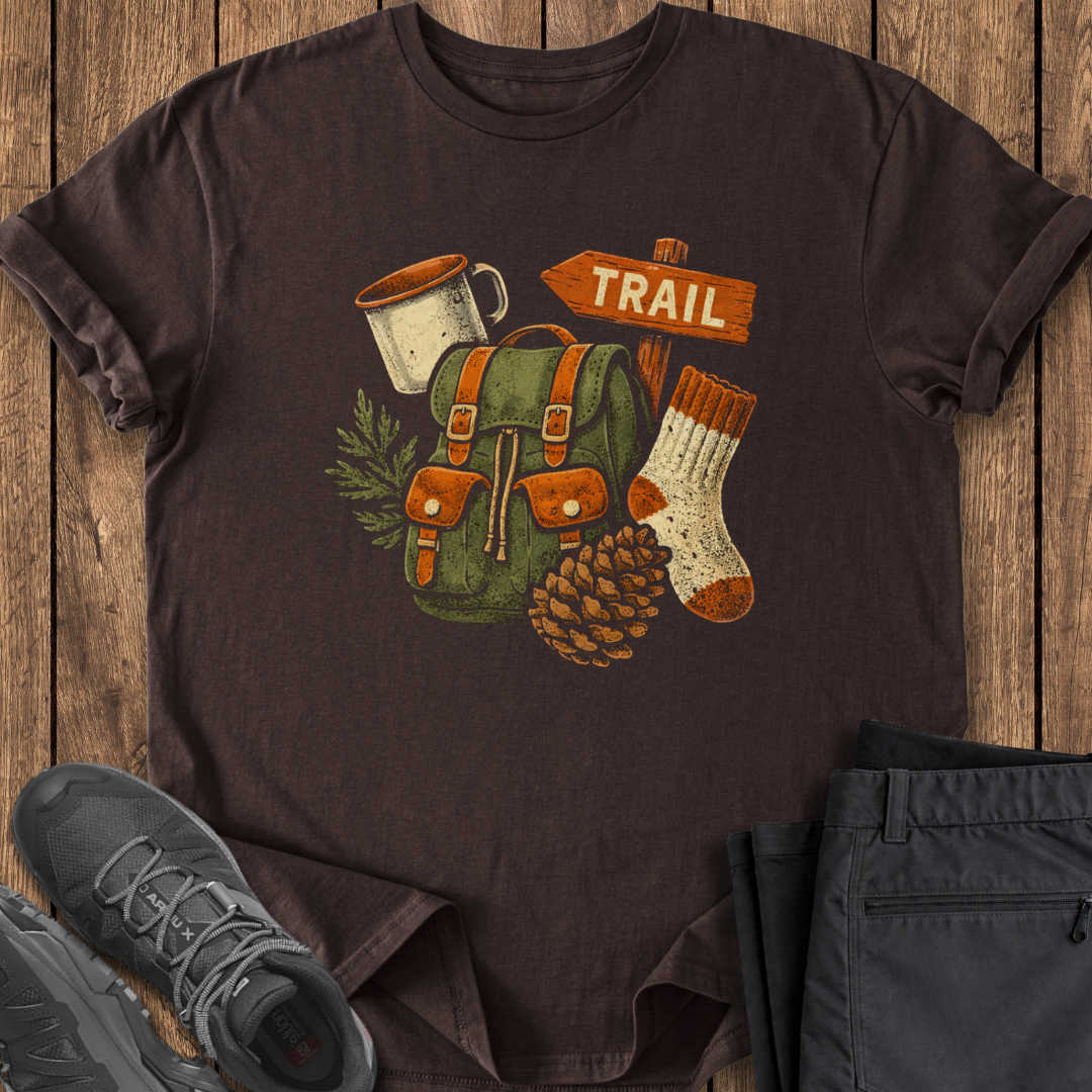 Brown t-shirt with outdoor-themed design on a wooden surface with shoes and pants.
