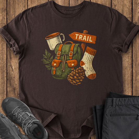 Brown t-shirt with outdoor-themed design on a wooden surface with shoes and pants.