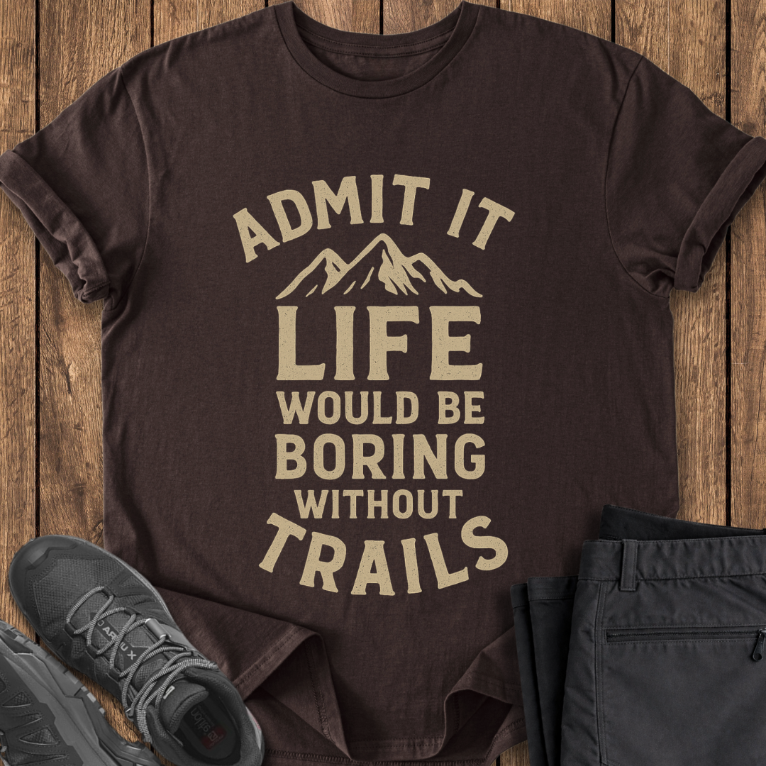 Brown t-shirt with 'Admit it, life would be boring without trails' text on a wooden surface with shoes and pants. hiking t shirt