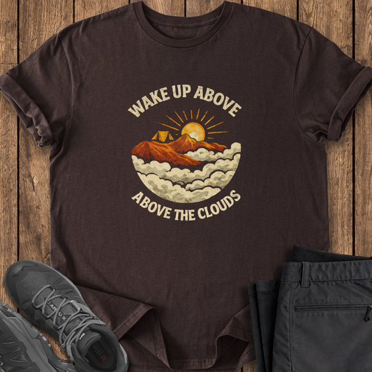 Brown t-shirt with mountain graphic and text on a wooden surface with shoes and pants. mountain climbing t shirt