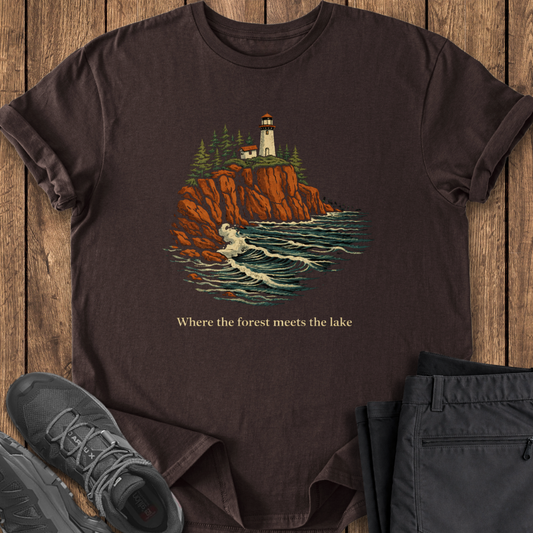 Brown t-shirt with a lighthouse design and text on a wooden surface, surrounded by shoes and pants. north shore lake supeior hiking 