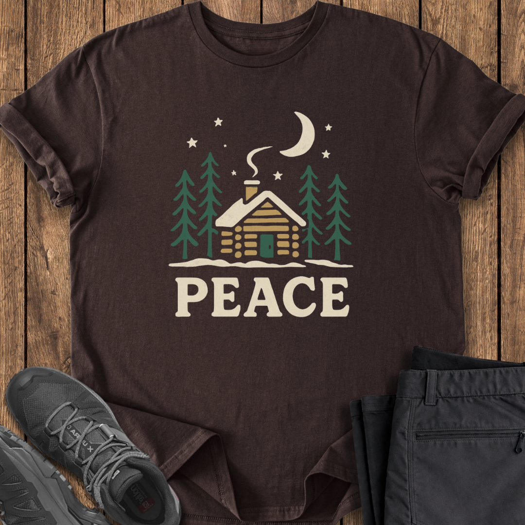 Brown t-shirt with a cabin and 'PEACE' design on a wooden surface with shoes and pants.