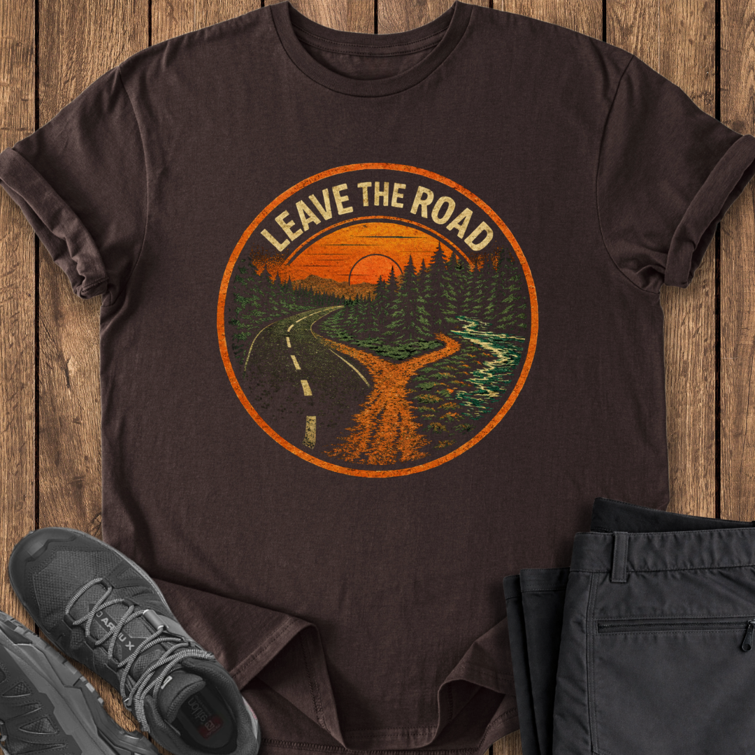 Brown t-shirt with 'Leave the Road' graphic on a wooden surface with shoes and pants.