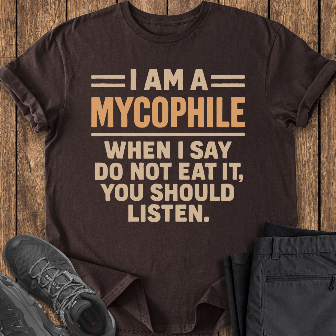Brown t-shirt with humorous text on a wooden surface with shoes and pants.