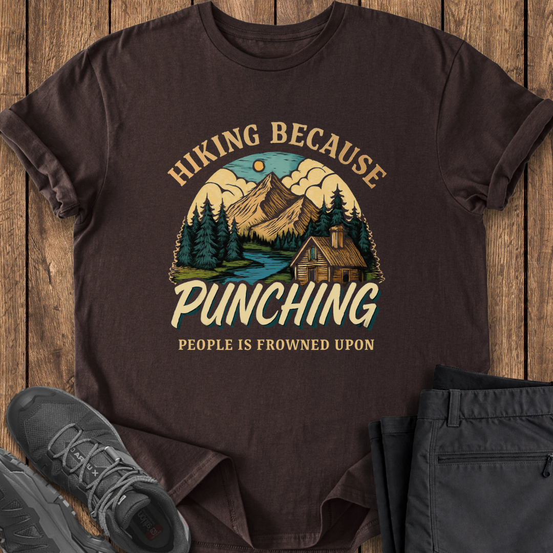 Brown t-shirt with hiking graphic and text on a wooden surface with shoes and pants. punching is frowned upon funny hiking shirt