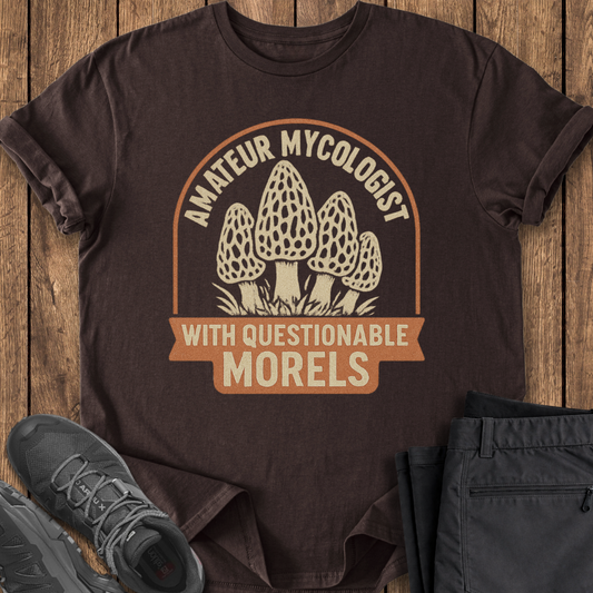 Brown t-shirt with mushroom graphic and text on a wooden surface, accompanied by black shoes and pants.